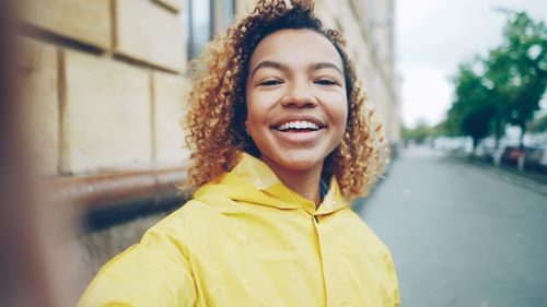 Free Joyful woman wearing a yellow raincoat, smiling on an urban street. Stock Photo