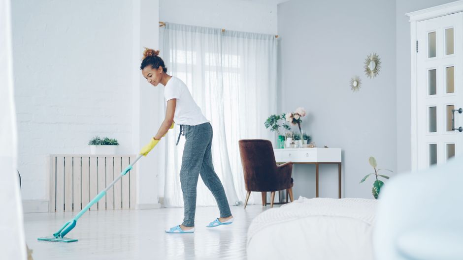 Mujer limpiando salón luminoso con fregona