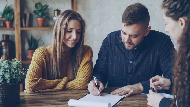 Three adults in a casual office setting reviewing and signing documents.
