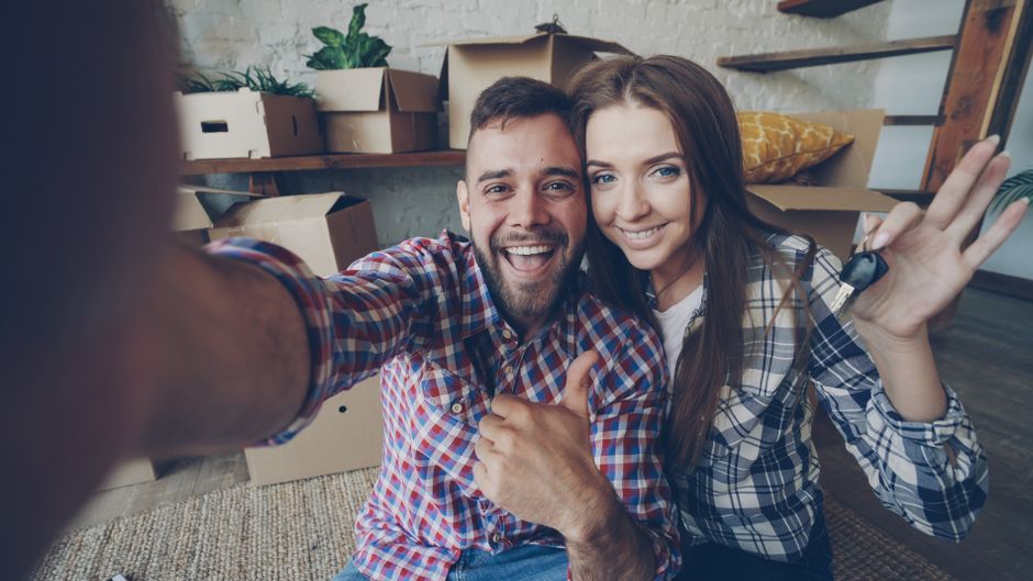 Una joven pareja celebra su nuevo hogar rodeados de cajas de mudanza.