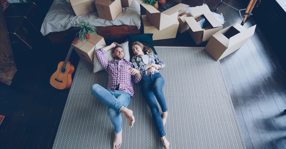 Happy couple lying on floor surrounded by moving boxes, signifying a new start.