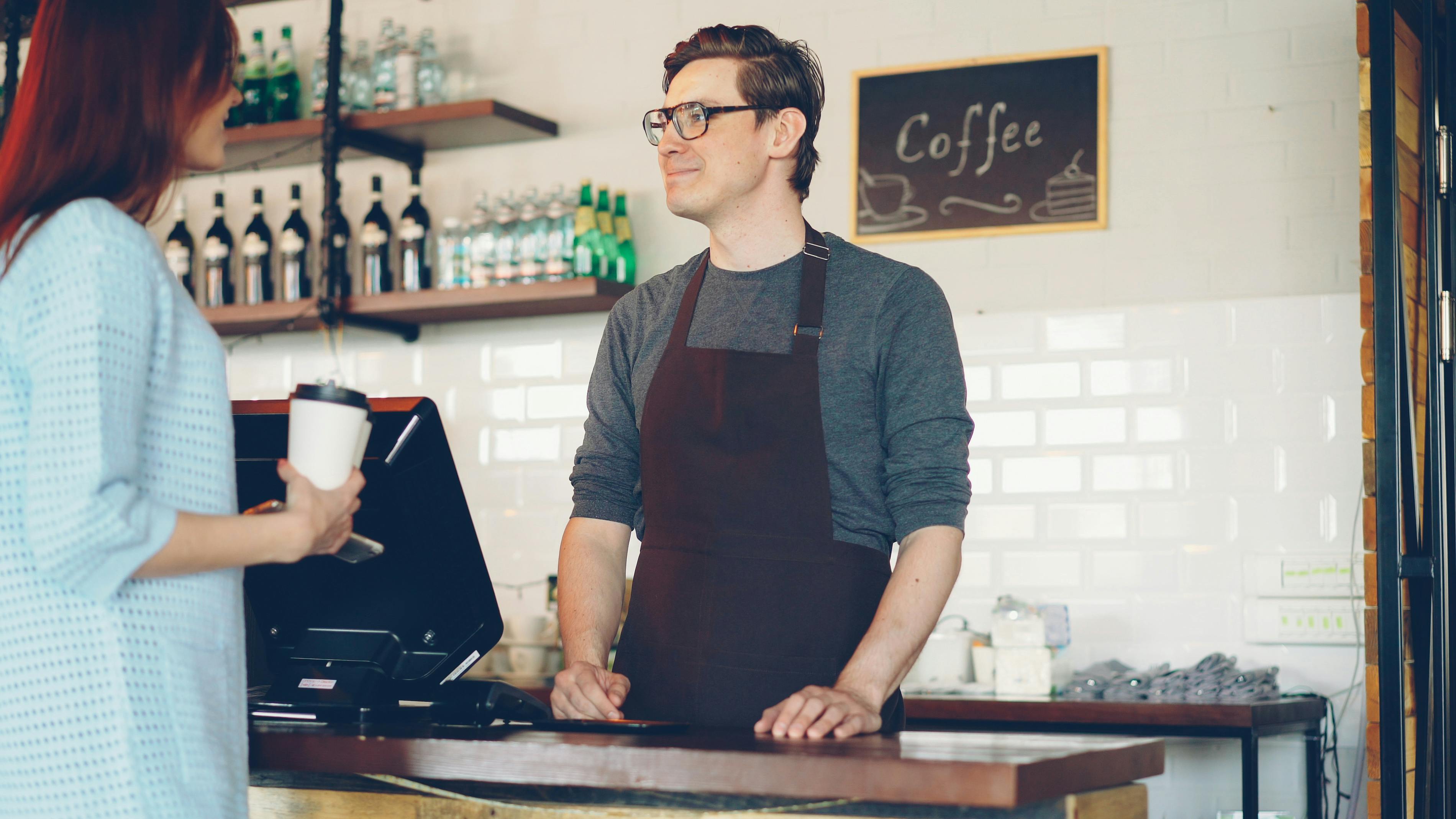 Barista in apron conversing with a customer at a cozy coffee shop counter.