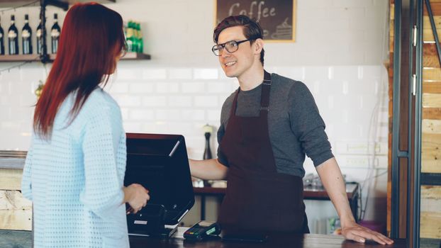 Smiling barista at counter helping a customer in a cozy cafe setting.