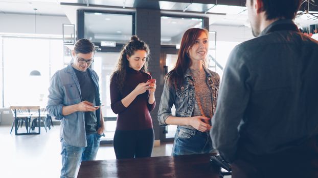 Three young adults in line at a café, interacting with the barista.