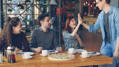 Free A group of friends celebrating with coffee and pizza in a lively cafe setting. Stock Photo