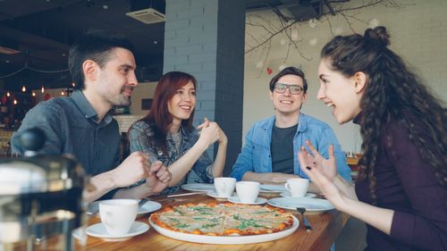 Free Group of four friends laughing and enjoying pizza and coffee together in a cozy cafe. Stock Photo