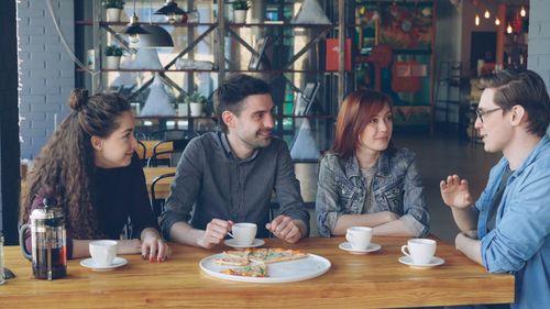 Free Group of young adults enjoying coffee and pizza in a trendy cafe. Stock Photo