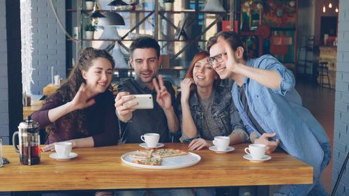 Free Group of friends taking a selfie while enjoying coffee and pizza in a cozy cafe. Stock Photo