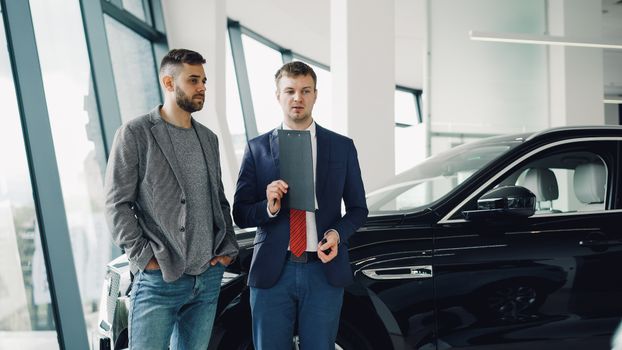 Two businessmen discussing car purchase in modern dealership showroom.