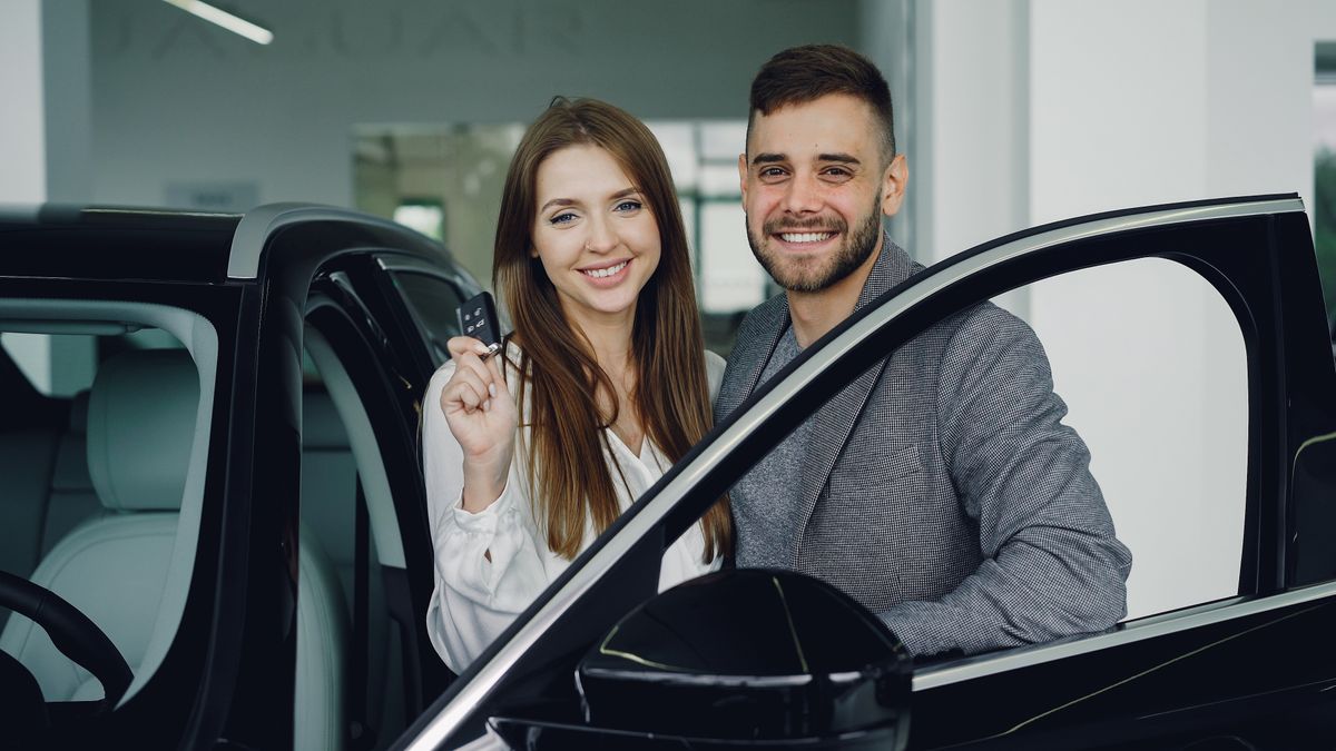 A happy couple in a car showroom holding the keys to their new vehicle