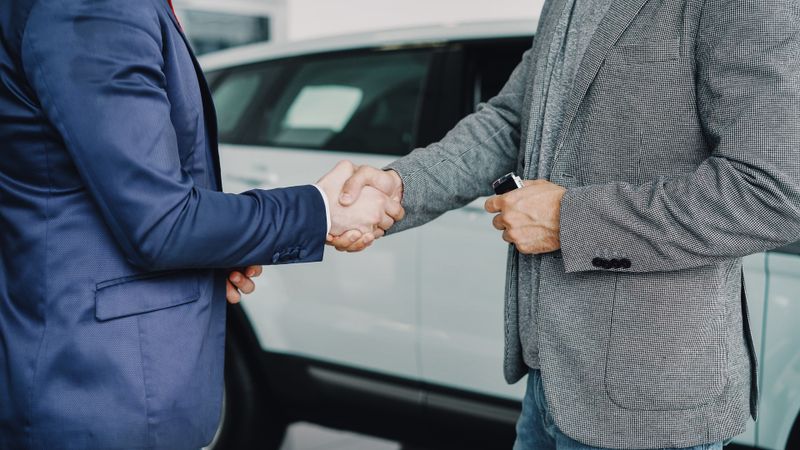 Two businessmen shaking hands in a car dealership sealing a deal