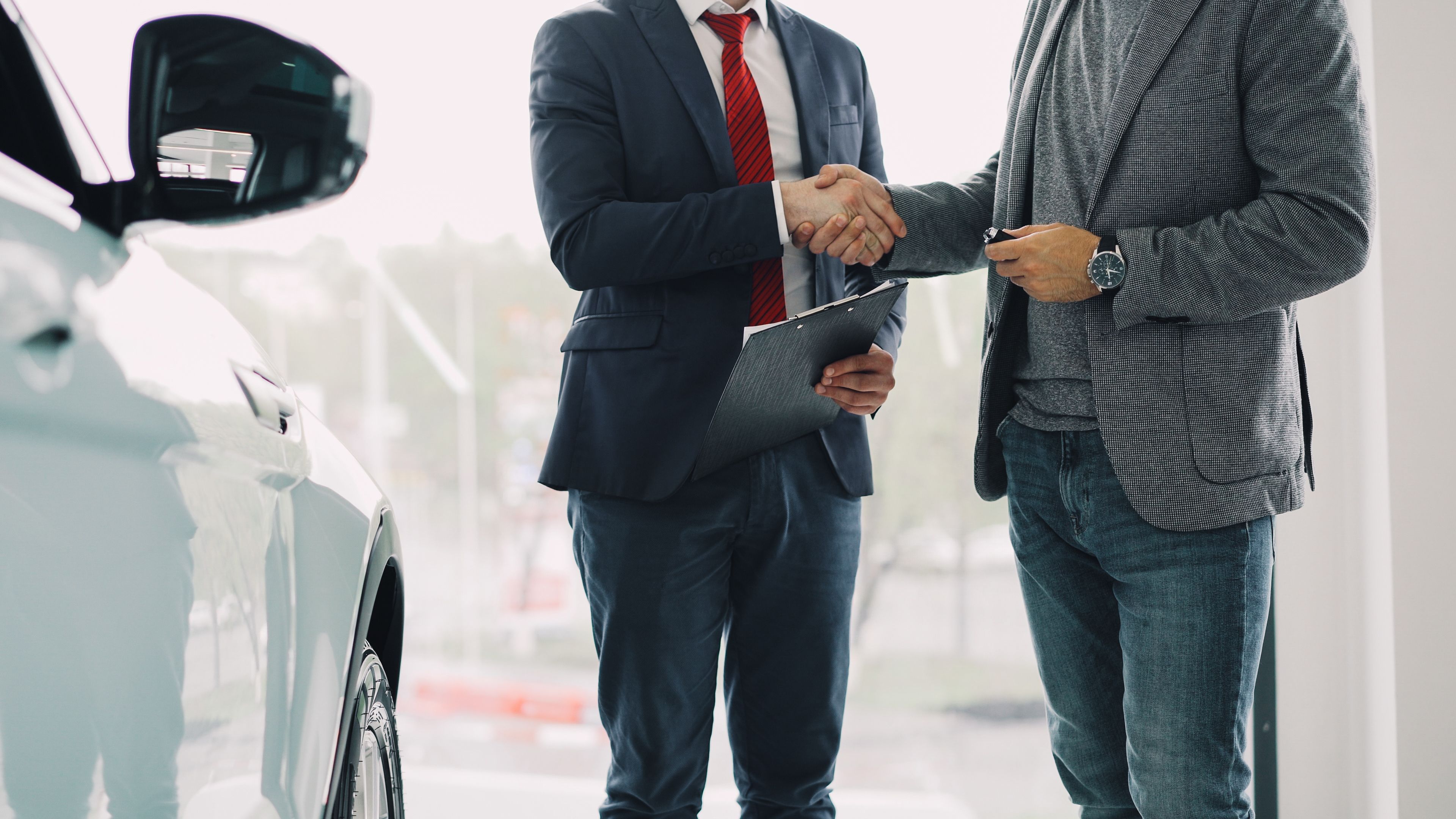 Two men shaking hands in a car dealership, symbolizing a successful business deal.