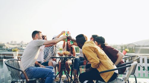 Free Friends enjoying a rooftop gathering with drinks, creating a lively and social atmosphere. Stock Photo