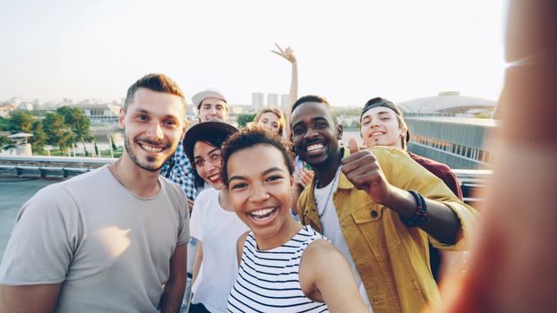 Diverse young friends smiling and posing for a rooftop selfie outdoors.