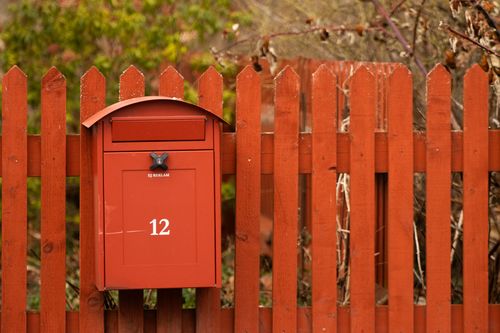 Free A red mailbox mounted on a matching wooden fence surrounded by vibrant greenery in Jönköping, Sweden. Stock Photo