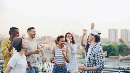 Free Happy group of friends enjoying a rooftop party with drinks, laughter, and dancing at sunset. Stock Photo