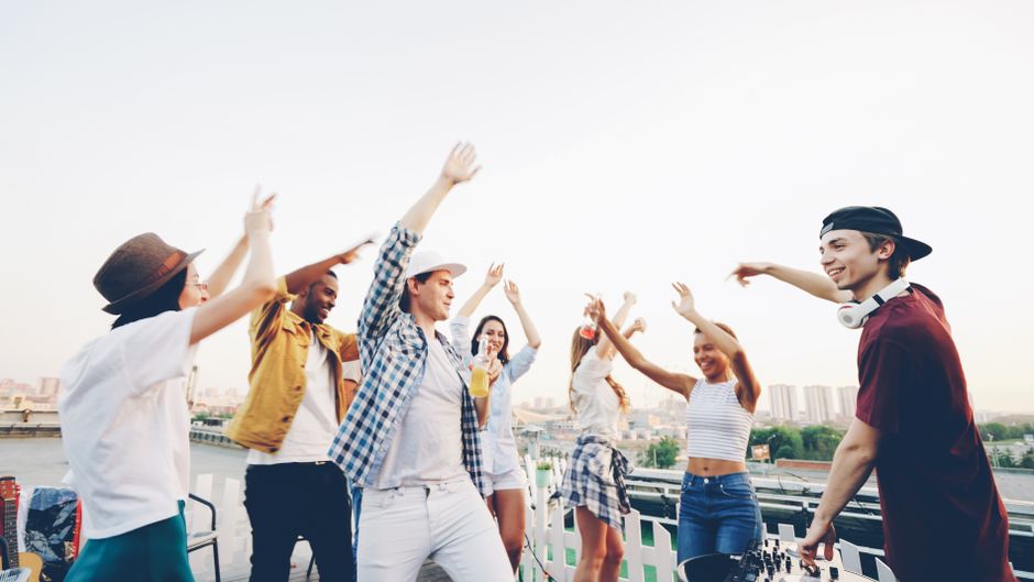 Group of friends dancing and celebrating on a rooftop with city skyline backdrop.