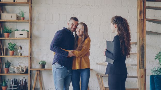 A joyful couple embraces as they make a real estate purchase with their realtor.
