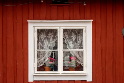 Free Red wooden house with a classic Swedish window featuring lace curtains and potted flowers. Stock Photo