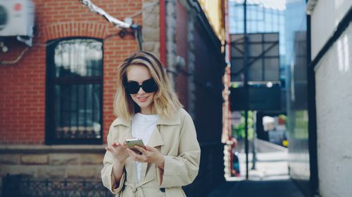 Free Stylish woman in sunglasses using smartphone in city alleyway. Stock Photo