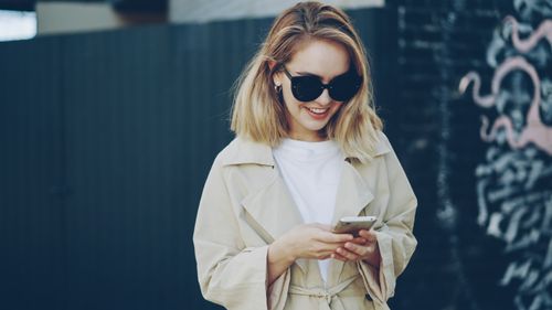 Free Fashionable woman in sunglasses using smartphone outdoors. Casual and modern style. Stock Photo