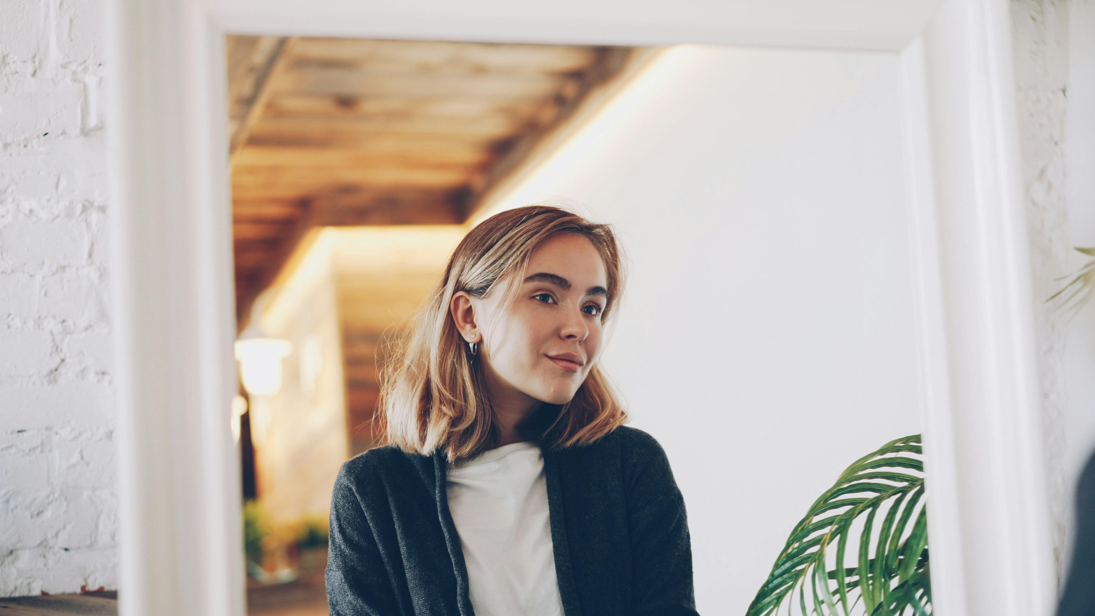 Reflective indoor portrait of a young woman in a cozy setting with soft lighting.