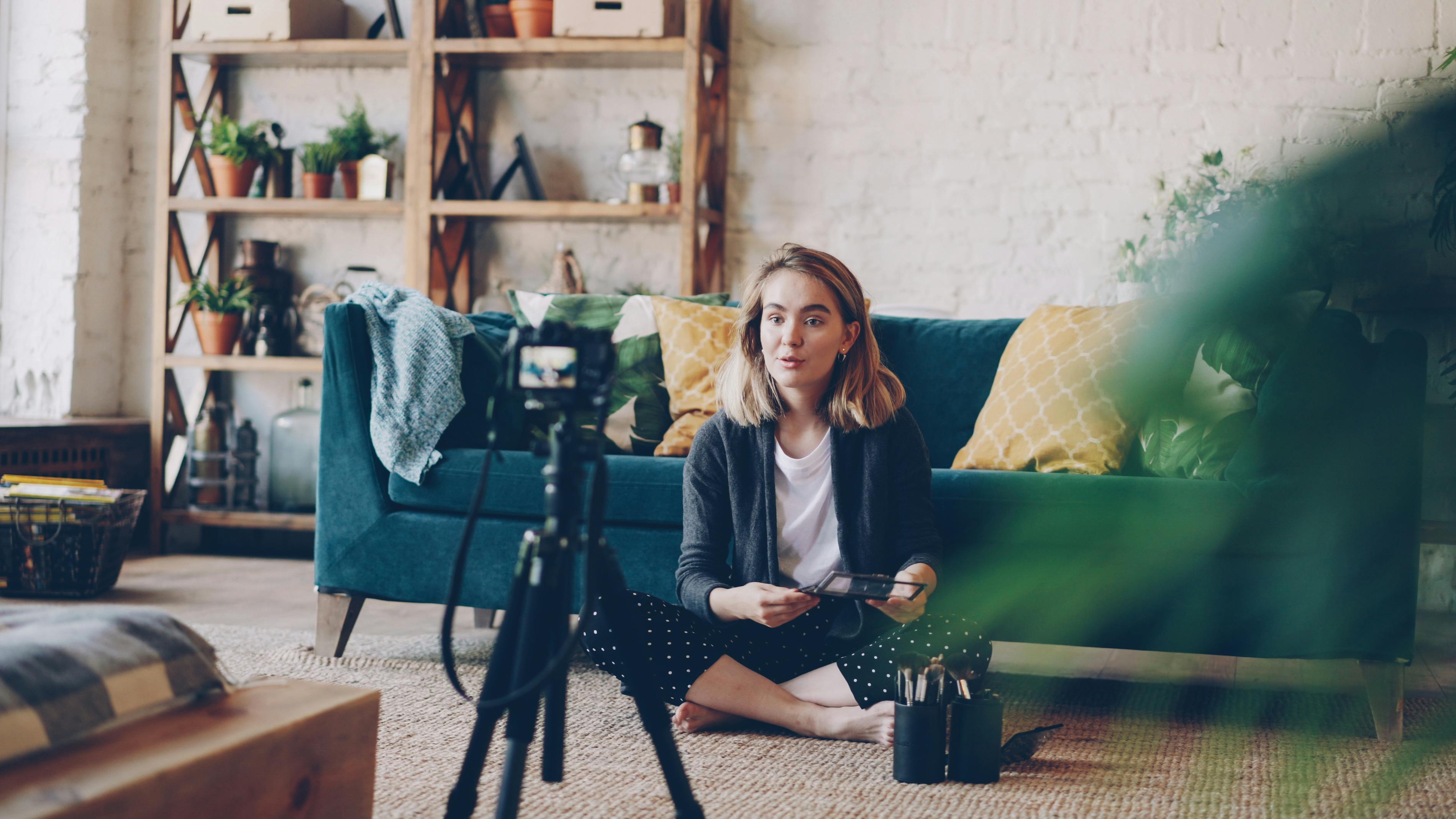 Woman filming vlog at home with camera setup, surrounded by plants and cozy decor.