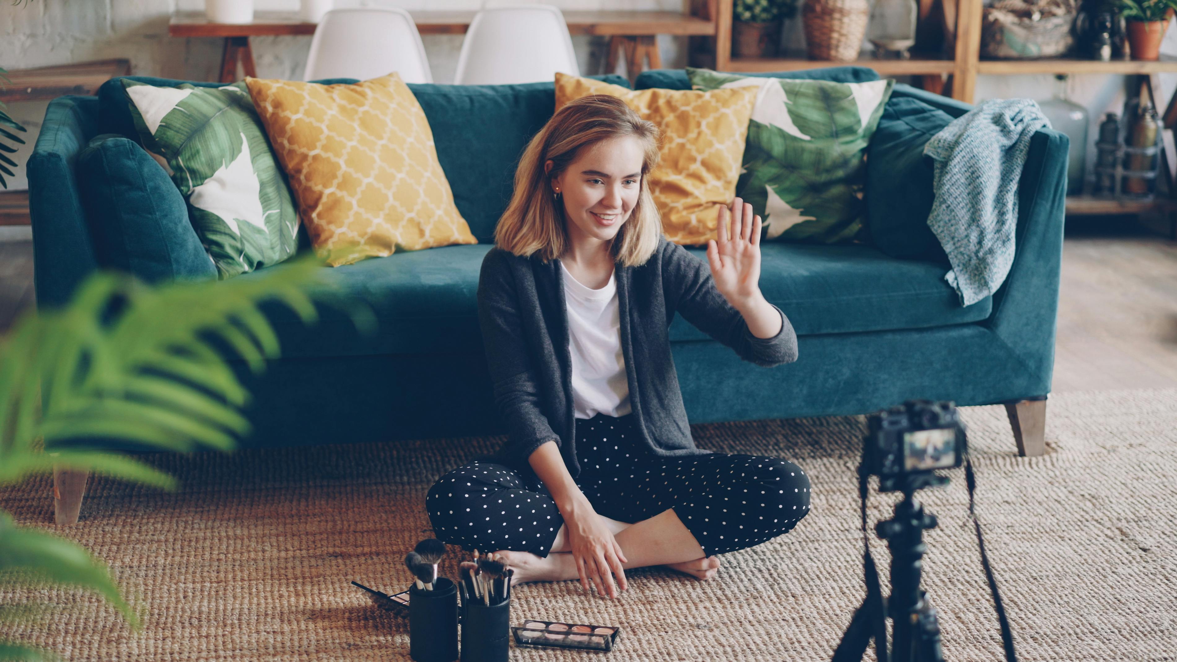 Smiling woman recording a vlog at home sitting on the floor.