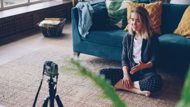 Young woman filming a vlog in a cozy, colorful living room setting.