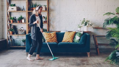 Free Woman wearing headphones, mopping floor in a cozy living room with plants. Stock Photo