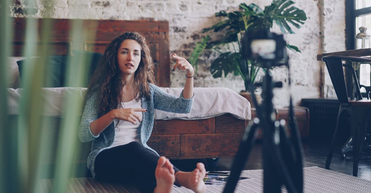 Woman sitting on floor filming vlog, discussing engaging topic. Home setting with cozy atmosphere.