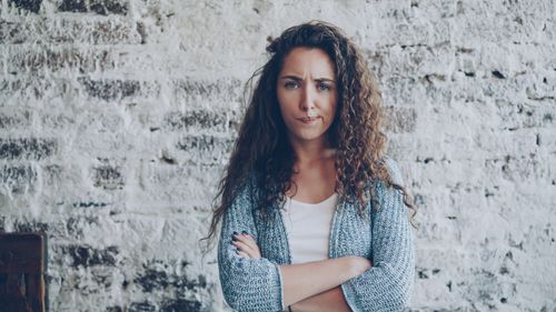 Free Portrait of a woman standing confidently with a textured brick background. Stock Photo