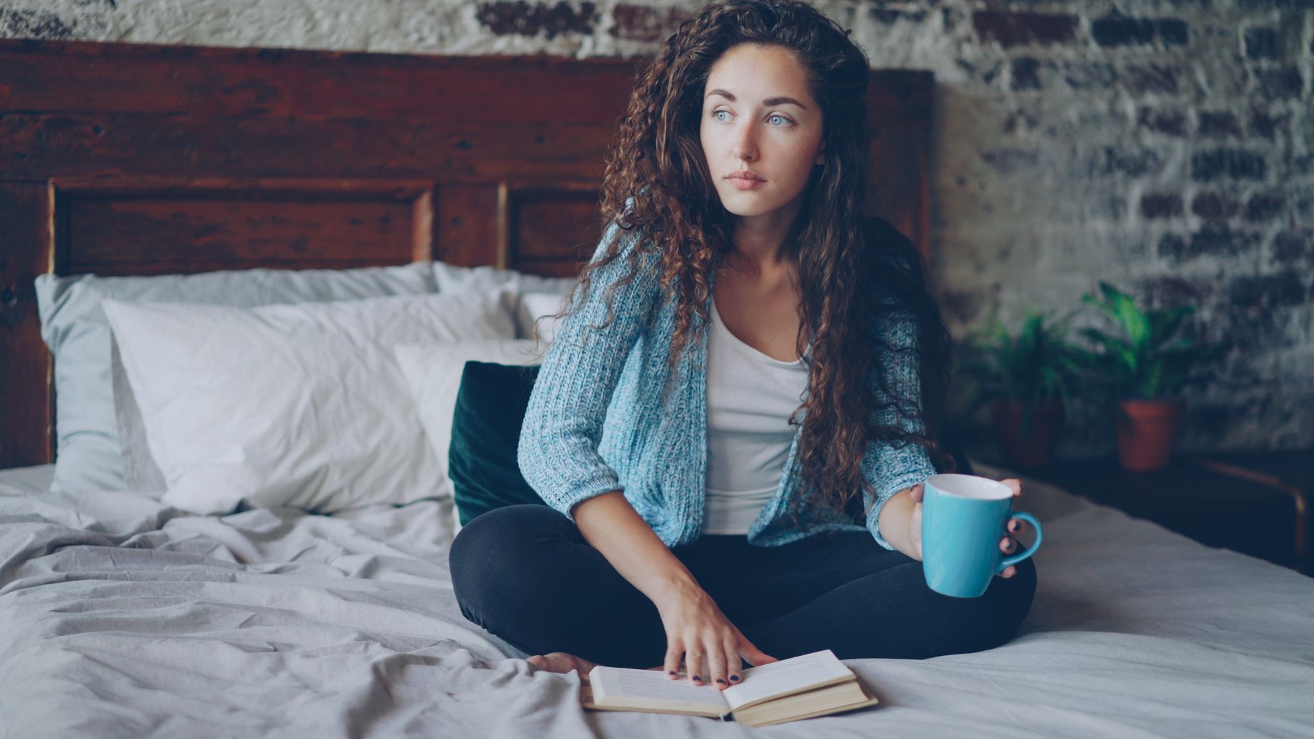 long covid brain fog recovery supplements — A young woman sits thoughtfully on her bed, holding a cup of coffee with an open notebook.