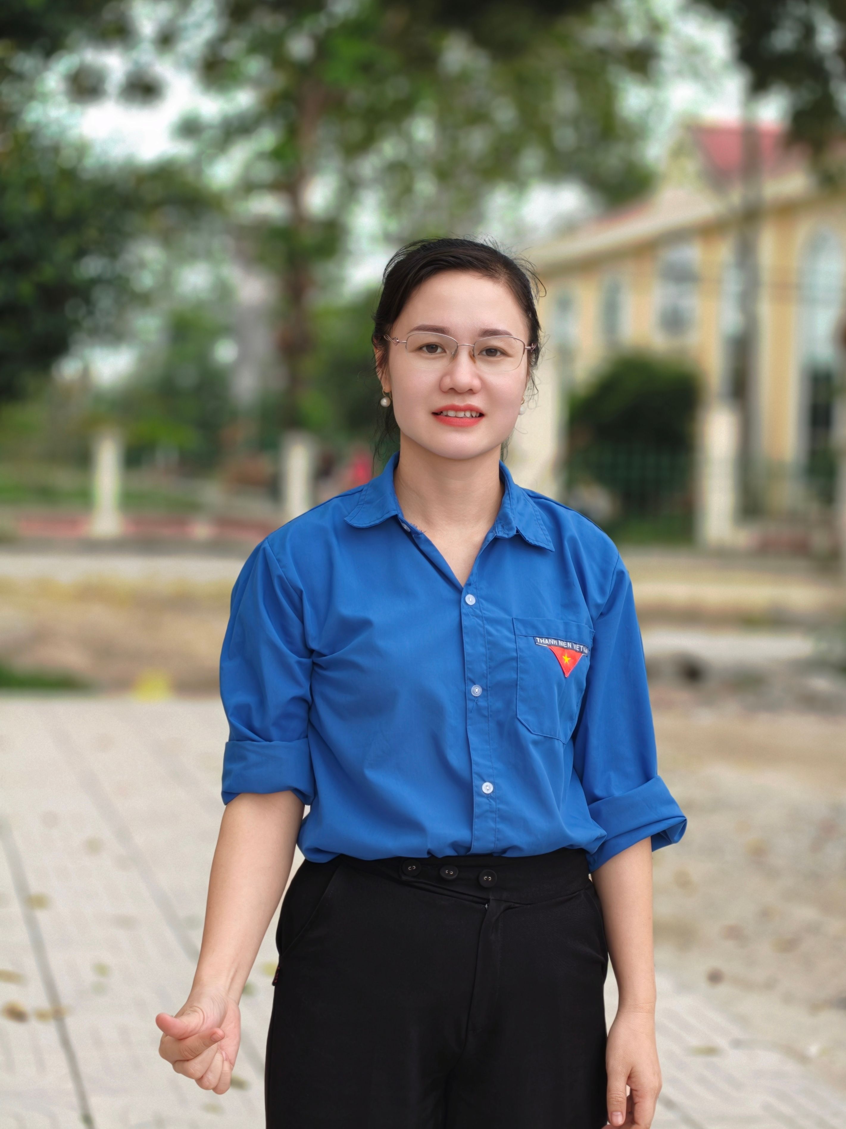 Portrait of a young woman in a blue shirt standing outdoors, smiling confidently.