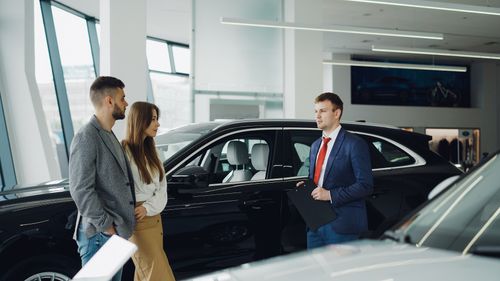 Free Salesperson assisting couple in modern car showroom. Stock Photo