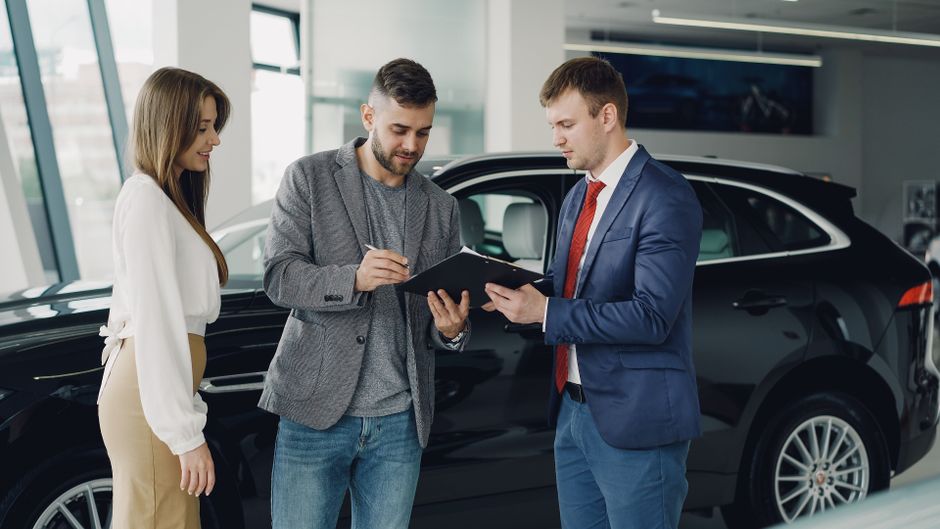 Three adults discussing documents at a car dealership beside