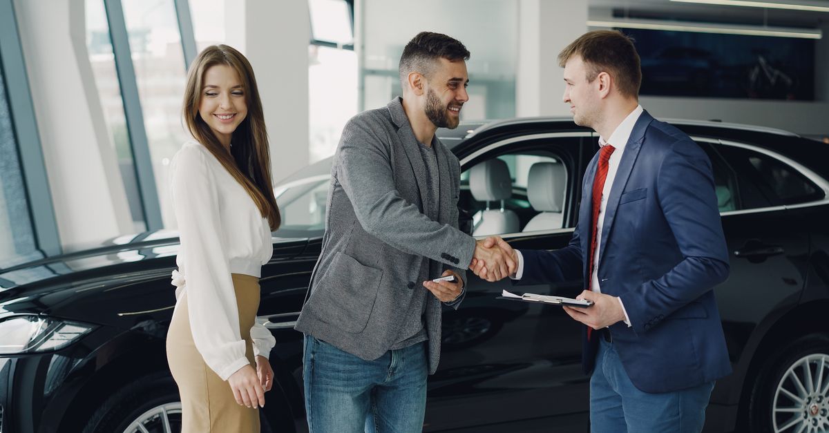 Buyers and sales representative shake hands at a car dealership for a successful car purchase.