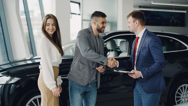 Buyers and sales representative shake hands at a car dealership for a successful car purchase.