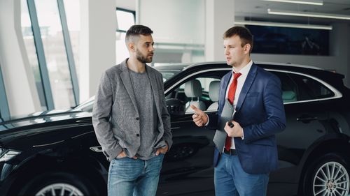 Free Two men discussing business in a car dealership, standing near a vehicle. Stock Photo