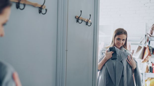 Smiling woman holding a coat in a boutique fitting room.