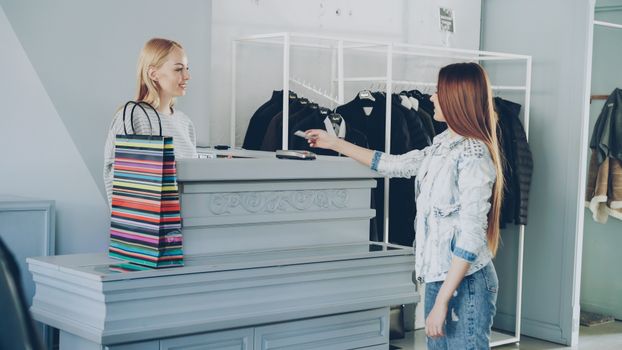 A woman paying by card at a store counter, handing card to female cashier.
