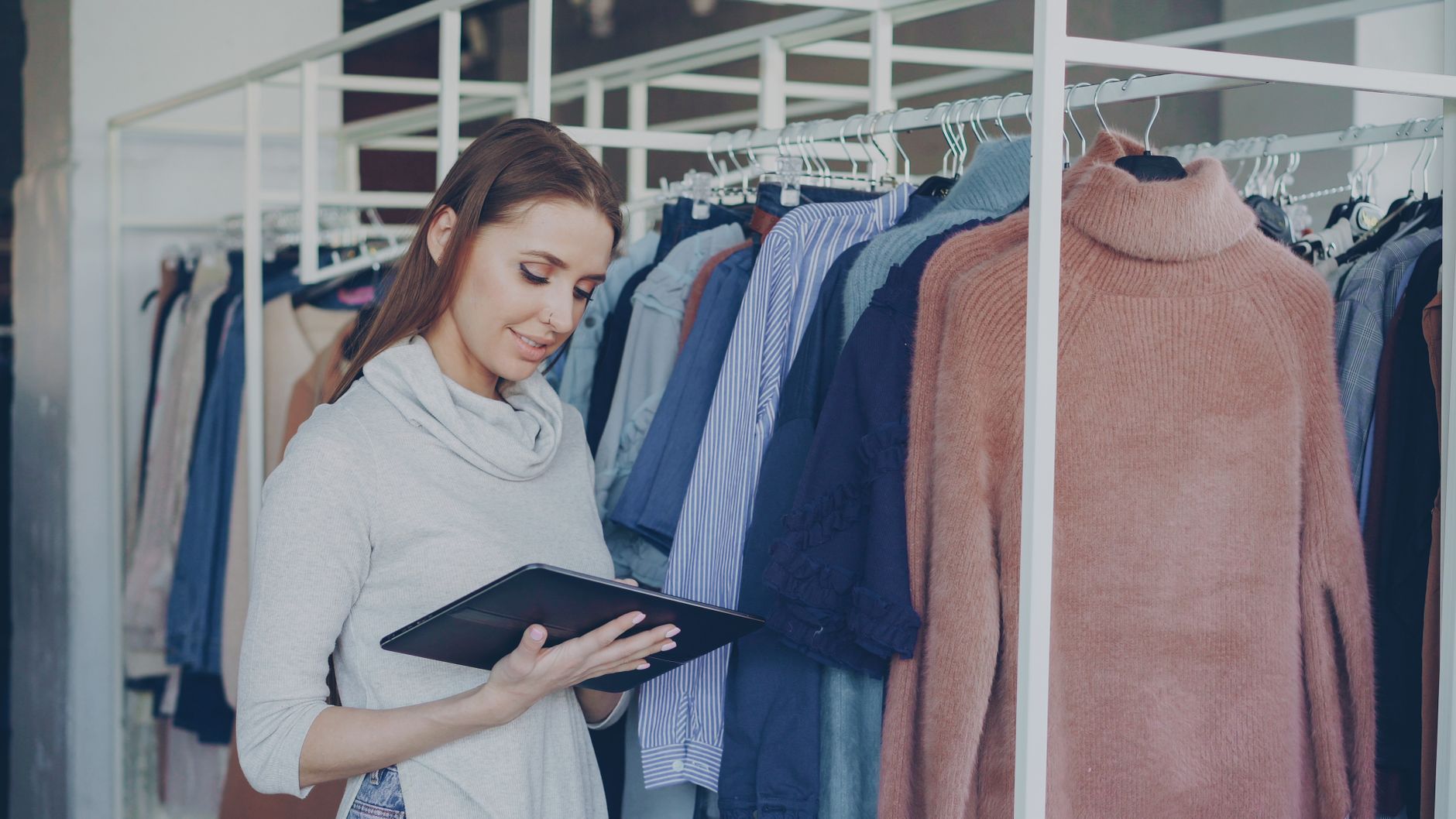 Female shop assistant using tablet to manage clothing inventory in a fashion boutique.