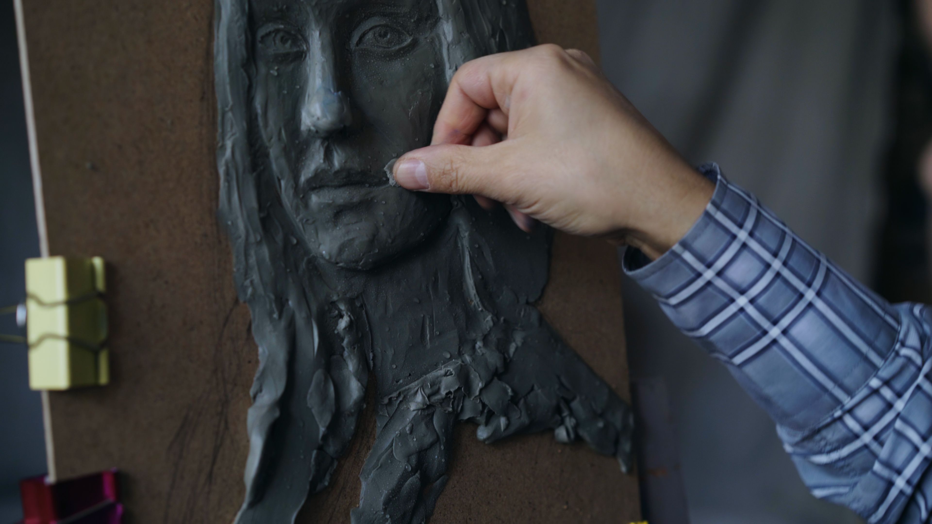 Close-up of an artist sculpting a clay face on a wooden board, creativity in action.