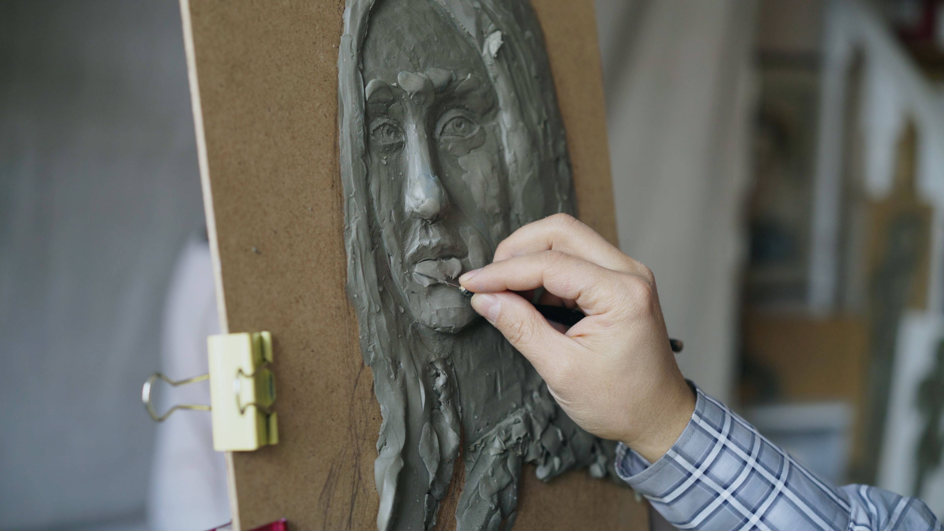 Close-up of an artist sculpting a detailed face in clay on a board.