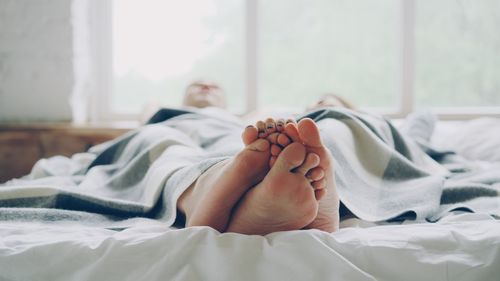 Free Cozy couple relaxing in bed under a warm blanket in soft daylight. Stock Photo