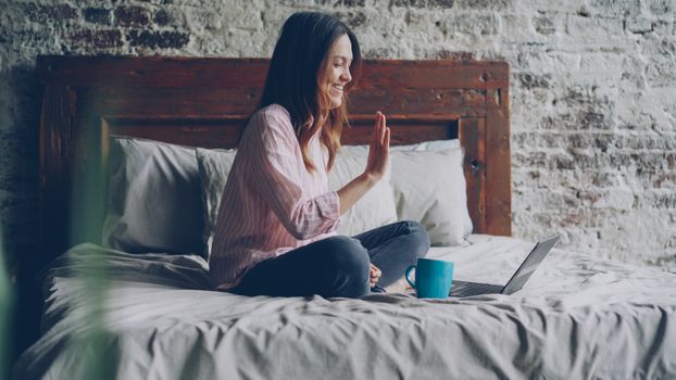 Woman sitting on bed video calling with laptop, cozy indoor setting.