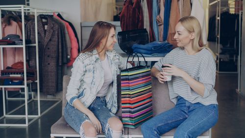 Free Two women enjoying a shopping break with colorful bags in a clothing store. Stock Photo
