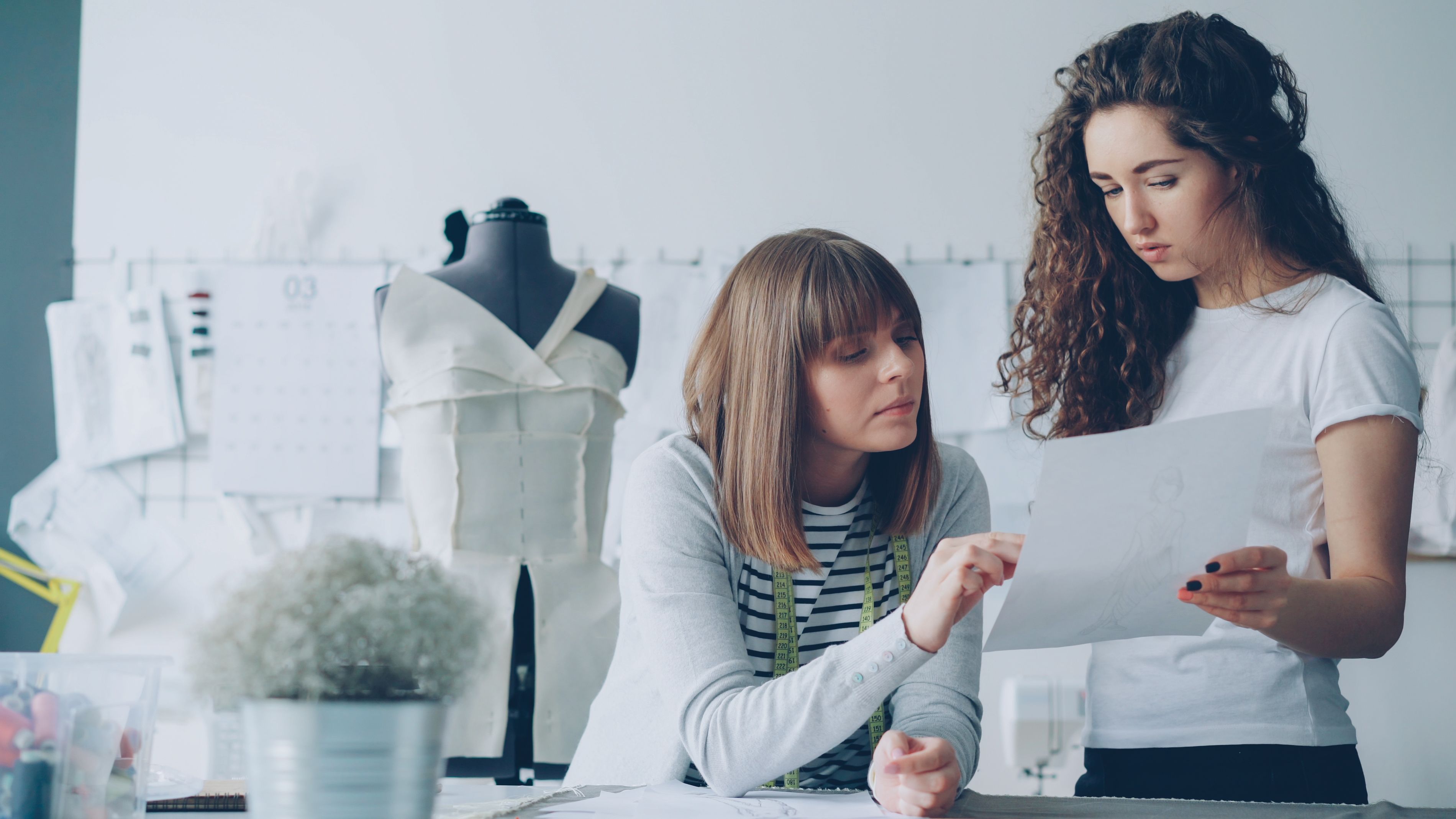 Two fashion designers discussing sketches in a bright studio.