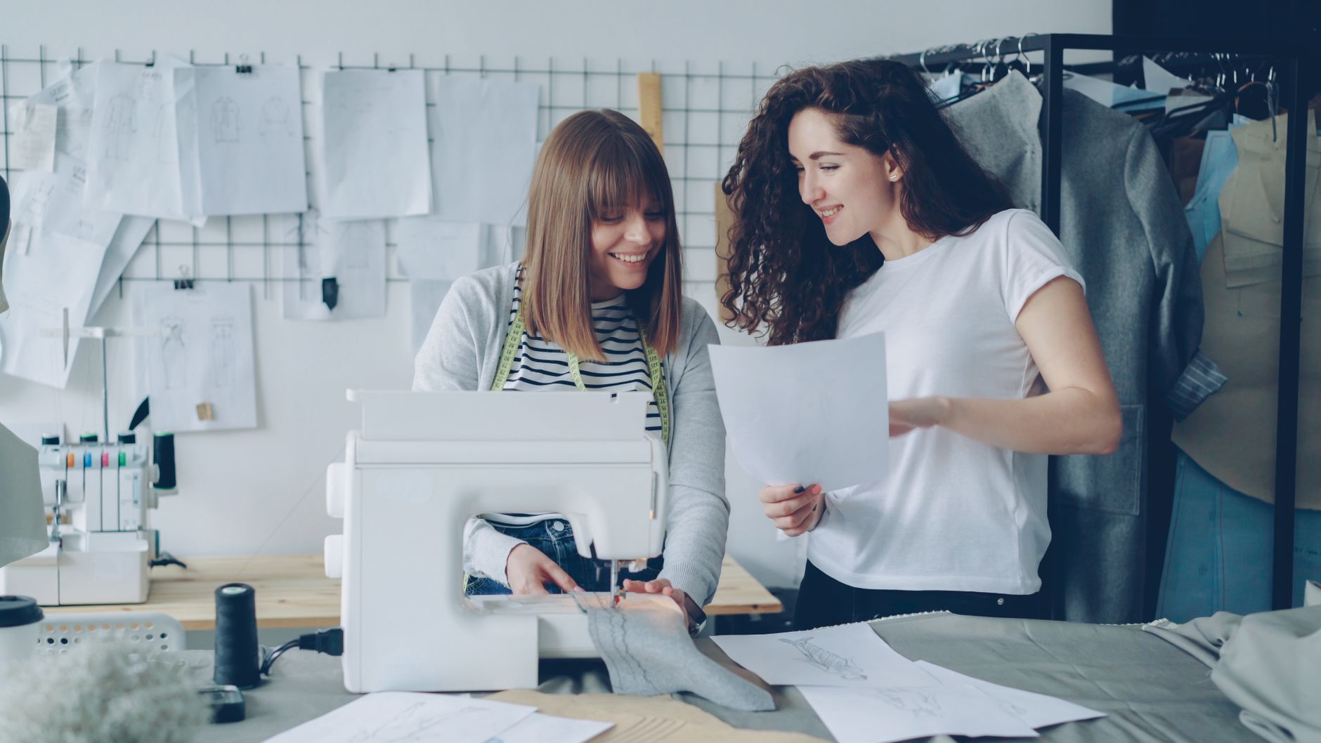Two women working together in a stylish fashion design studio with sewing machine and sketches.