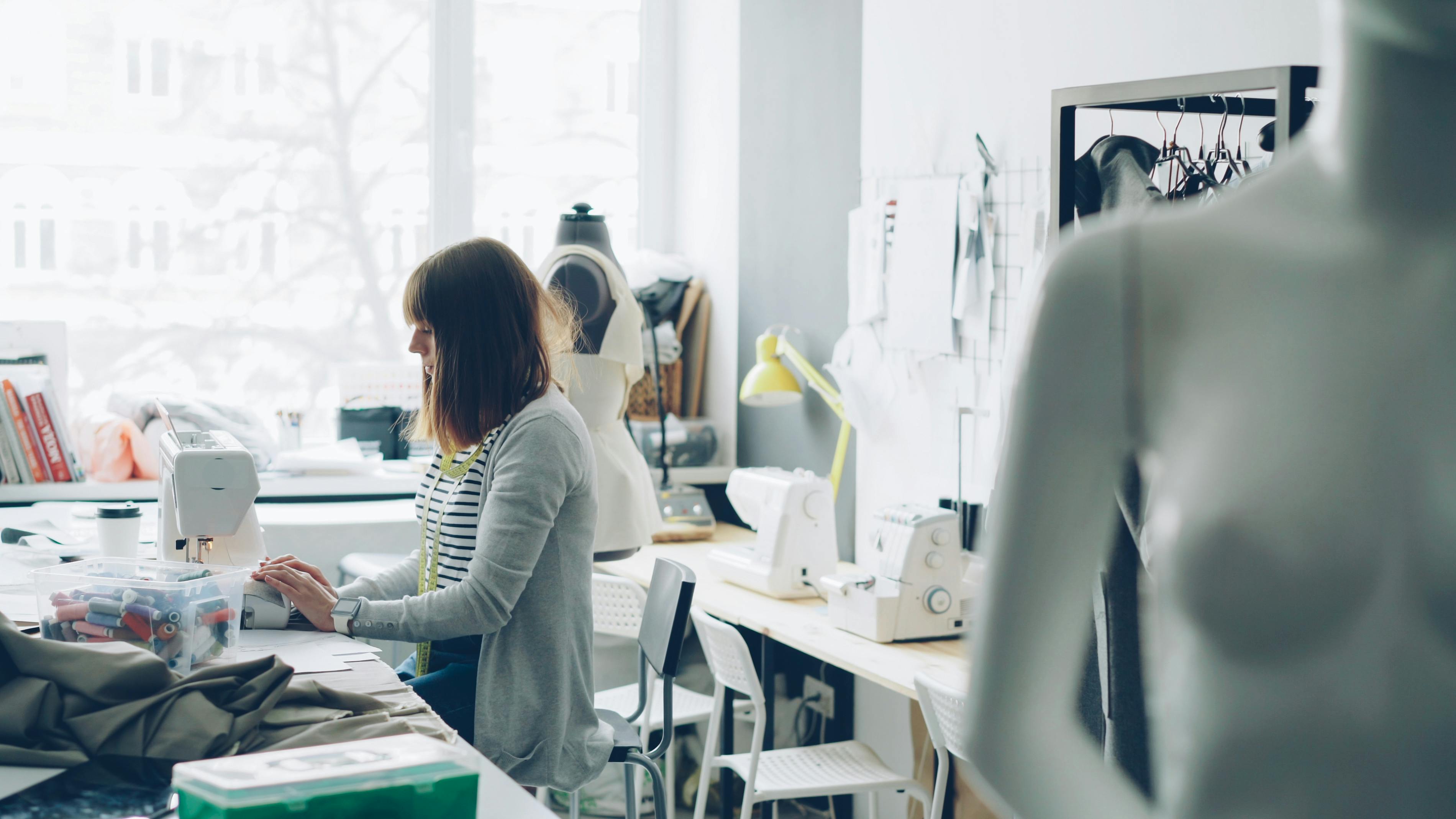 Female fashion designer working at sewing machine in bright studio.